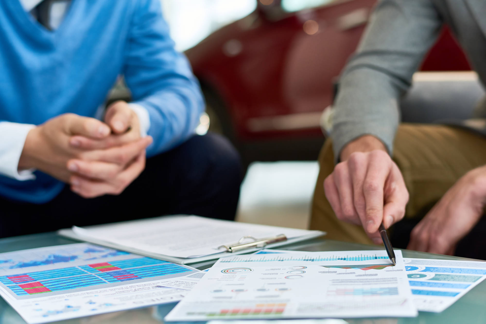 Close up of two unrecognizable young men discussing marketing strategies and marketing  data sitting at coffee table with charts and graphs